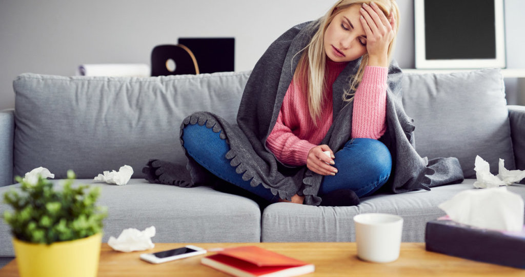 Sick woman with headache sitting under the blanket in living room