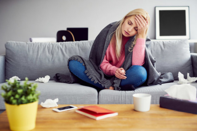 Sick woman with headache sitting under the blanket in living room